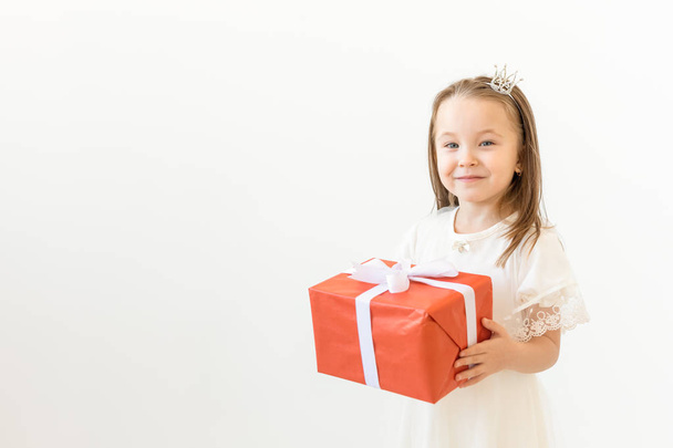 people, children and holiday concept - portrait of happy little girl holding a gift box over white background with copy space - Photo, Image