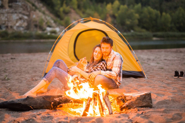 mensen, zomer toerisme en natuur concept - paar in de buurt van camp vuur opwarmen gezien vanaf de tent - Foto, afbeelding