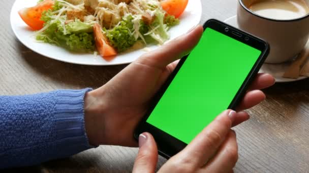 Πλήκτρο αποχρώσεων ή πράσινη οθόνη σε μαύρο smartphone σε γυναικεία χέρια με καλά καλλωπισμένο μανικιούρ στο φόντο μιας σαλάτας του Καίσαρα και φλιτζάνι καφέ σε ένα εστιατόριο - Πλάνα, βίντεο