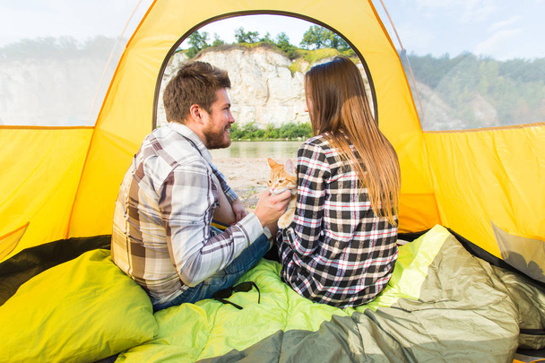 People, tourism and nature concept - Cute couple sitting with a cat in yellow tent - Photo, Image