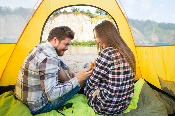 People, tourism and nature concept - Cute couple sitting with a cat in yellow tent - Photo, Image