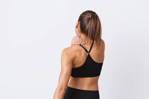 Frau massiert Schmerzen zurück. sportliches Mädchen mit Rückenschmerzen, auf weißem Wandhintergrund  - Foto, Bild
