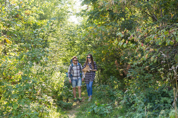 Reizen, avonturen, wandeling, toerisme en natuur concept - toeristische paar met kat lopen in het bos - Foto, afbeelding
