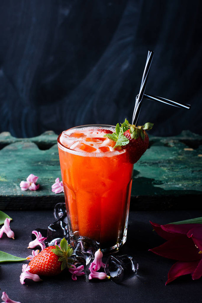 Refroidir le jus de fraise frais dans un verre avec des fruits et de la paille sur fond de table sombre
  - Photo, image