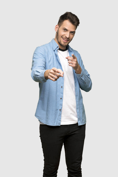 Handsome man points finger at you while smiling over grey background - Foto, afbeelding