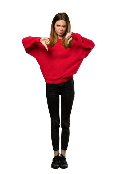 A full-length shot of a Young woman with red sweater showing thumb down over isolated white background - Photo, Image