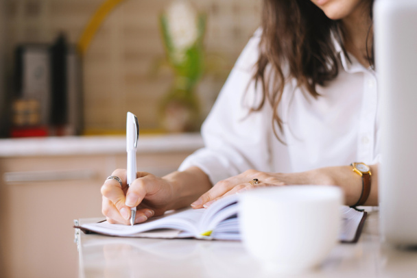 Close up de uma mulher escritor mão escrever em um notebook em casa na cozinha
 - Foto, Imagem