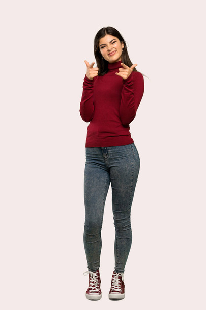 A full-length shot of a Teenager girl with turtleneck pointing to the front and smiling over isolated background - Photo, image