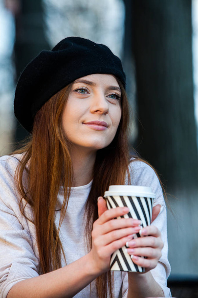 Hermosa joven con una taza de café en la calle de la ciudad. Descanso. Café para llevar. Elegante chica hipster bebiendo café en la calle
. - Foto, imagen