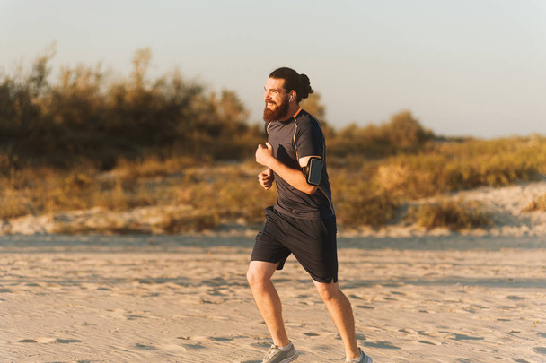Бородатий чоловік тренується на тропічному пляжі вранці. Молода людина вранці біжить на відкритому повітрі
. - Фото, зображення