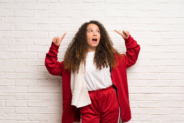 Teenager sport girl with curly hair pointing up and surprised - Photo, Image