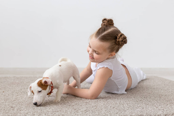 Koncepcja zwierzętom, dzieciństwa i zwierząt - małe dziecko dziewczynka gra na podłodze z szczeniak Jack Russell Terrier - Zdjęcie, obraz