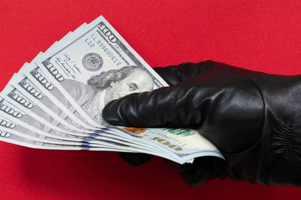 Hand in black glove holding money. Red background. Close Up. - Foto, imagen