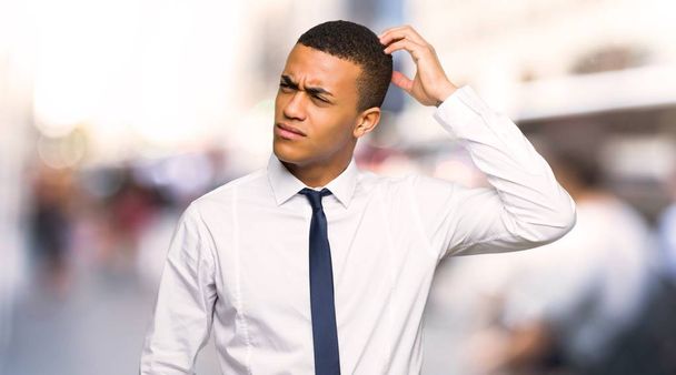 Joven empresario afroamericano que tiene dudas mientras se rasca la cabeza en la ciudad
 - Foto, Imagen