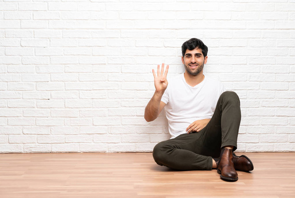 Young man sitting on the floor happy and counting four with fingers - Foto, Bild