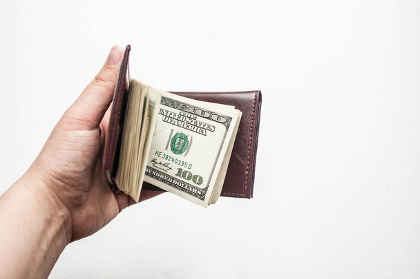 Women hand holding a wallet full of one hundred dollar bills isolated over a white background. - Фото, изображение