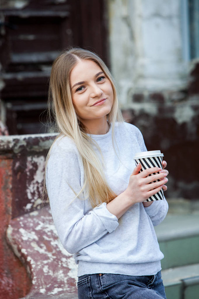 Gorgeous young woman with cup of coffee in city street. Coffee break. Coffee to go.Stylish hipster girl drinking coffee in street. - Foto, afbeelding