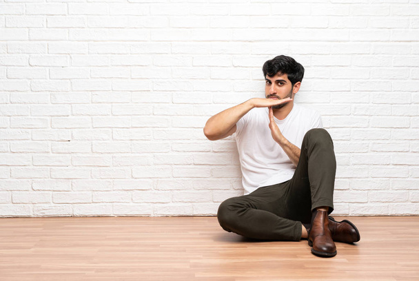 Jonge man zittend op de vloer time-out gebaar maken - Foto, afbeelding