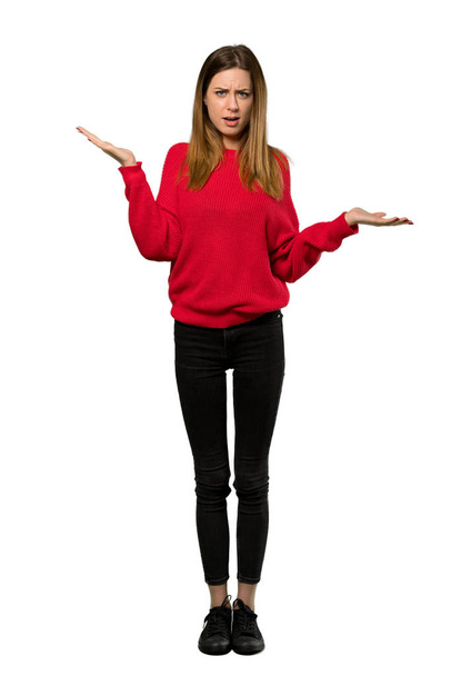 Een full-length schot van een jonge vrouw met rode trui ongelukkig omdat iets niet begrijpen over geïsoleerde witte achtergrond - Foto, afbeelding