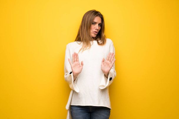 Mulher loira sobre a parede amarela fazendo parar gesto com ambas as mãos
 - Foto, Imagem