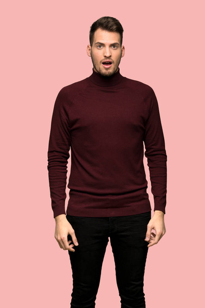 Man with turtleneck sweater surprised and shocked while looking right over pink background - Zdjęcie, obraz