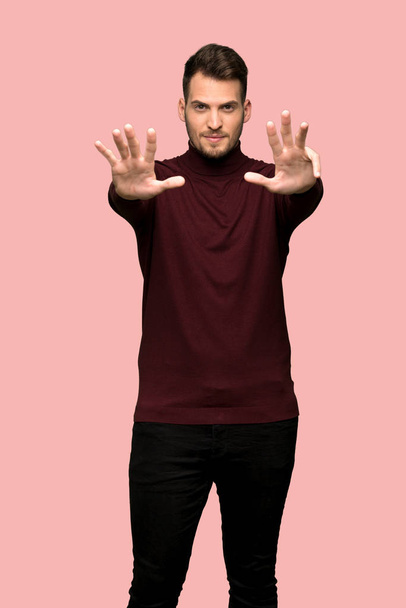 Mies, jolla on poolopaita, laskee yhdeksän sormea vaaleanpunaisen taustan päällä
 - Valokuva, kuva