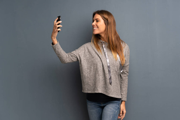 Blondine vor grauem Hintergrund macht ein Selfie - Foto, Bild