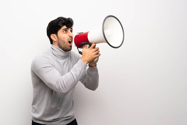 Mladý muž nad izolované bílé zdi křičí přes megafon - Fotografie, Obrázek