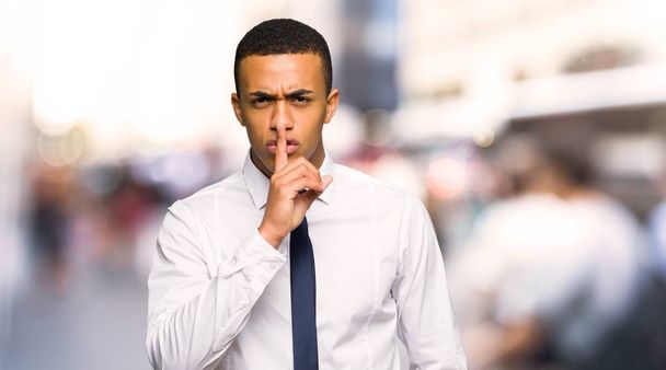 Молодой афро-американский бизнесмен показывает знак молчания жест положить палец в рот в городе
 - Фото, изображение