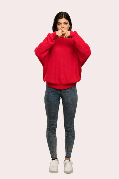 A full-length shot of a Teenager girl with red sweater showing a sign of silence gesture over isolated background - Φωτογραφία, εικόνα