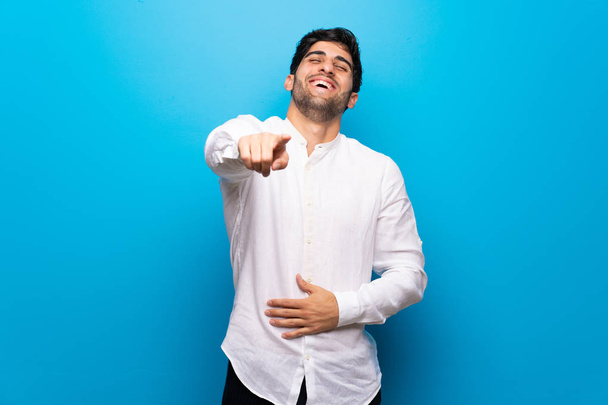 Молодий чоловік над ізольованою синьою стіною вказує пальцем на когось і багато сміється
 - Фото, зображення