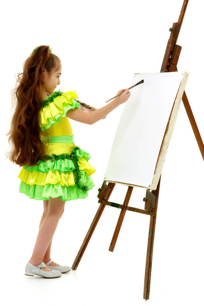 Little girl with a palette and brush near the easel. - 写真・画像