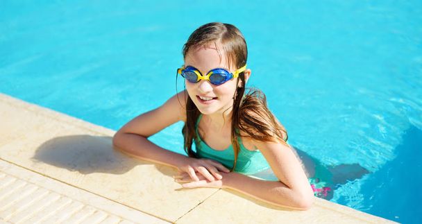 Cute young girl wearing swimming goggles having fun in outdoor pool. Child learning to swim. Kid having fun with water toys. Family fun in a pool. - Foto, Imagen