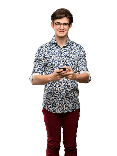 Teenager man with flower shirt and glasses sending a message with the mobile over isolated white background - Foto, immagini