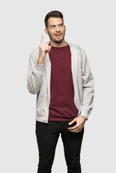 Man with sweatshirt intending to realizes the solution while lifting a finger up over grey background - Foto, immagini