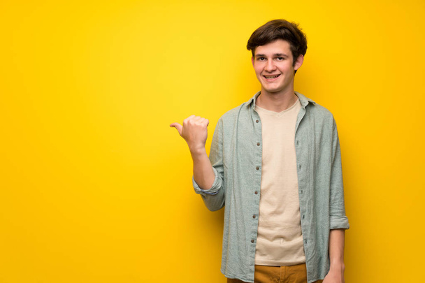 Teenager man over yellow wall pointing to the side to present a product - Photo, image