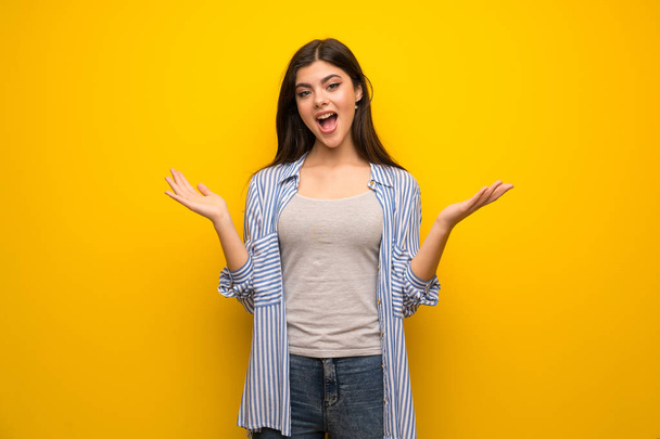 Menina adolescente sobre a parede amarela com expressão facial chocada
 - Foto, Imagem