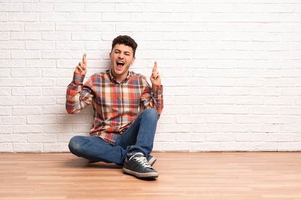 Mladý muž sedí na podlaze s prsty přes - Fotografie, Obrázek