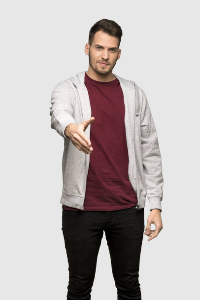 Man with sweatshirt shaking hands for closing a good deal over grey background - Photo, image