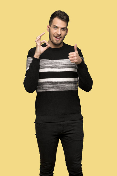 Handsome man showing ok sign with and giving a thumb up gesture over yellow background - Photo, Image