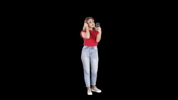 Mooie jonge vrouw met behulp van mascara en op zoek in haar smartphone, Alpha Channel - Video