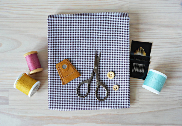 Checked fabric, leather thimble, retro scissors, wooden buttons, quilting needles and colorful threads on the table - Fotoğraf, Görsel