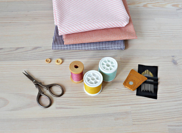Bobinas de hilo de colores, botones de madera, dedal de cuero, tijeras retro, telas de algodón y agujas de acolchado en la mesa
 - Foto, imagen