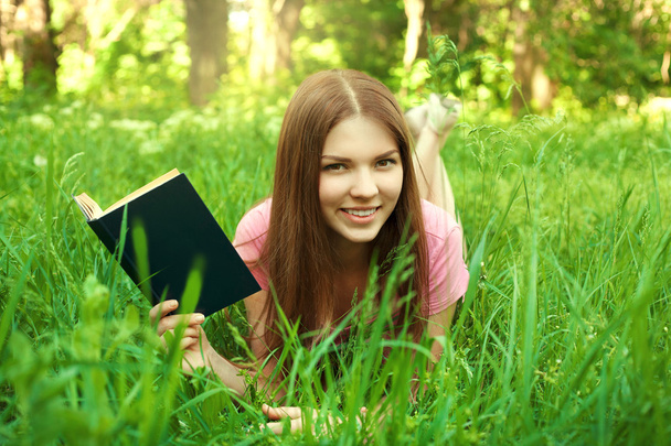 クローズ アップの女の子、公園で本を読んでの笑みを浮かべて肖像画 - 写真・画像