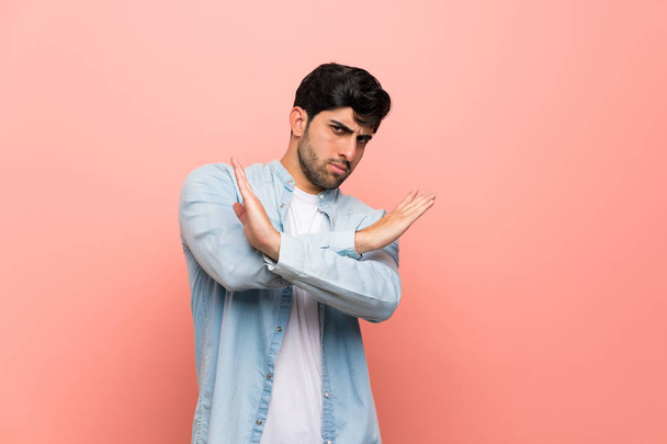Young man over pink wall making NO gesture - 写真・画像