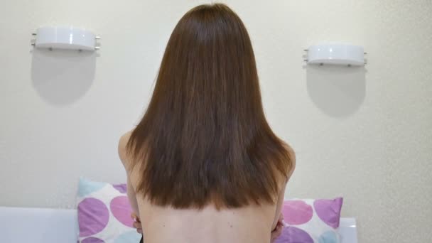 Vista posterior de la atractiva mujer adulta en topless con el pelo largo y castaño sentado en la cama en su casa. Concepto de cuerpo desnudo
 - Metraje, vídeo