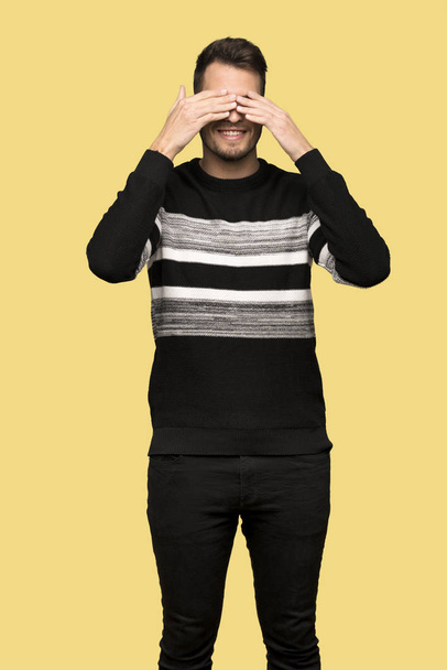 Handsome man covering eyes by hands. Surprised to see what is ahead over yellow background - Photo, Image