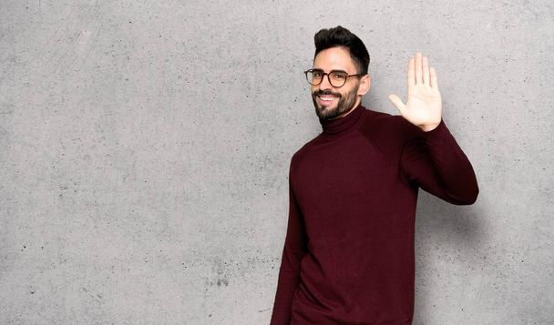 Handsome man with glasses saluting with hand with happy expression over textured wall - Photo, Image