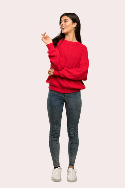 A full-length shot of a Teenager girl with red sweater pointing finger to the side over isolated background - Фото, изображение