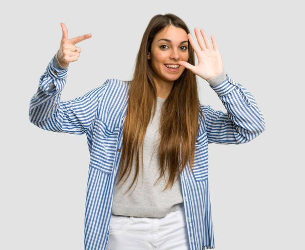 Chica joven con camisa a rayas contando siete con los dedos sobre fondo gris aislado
 - Foto, imagen